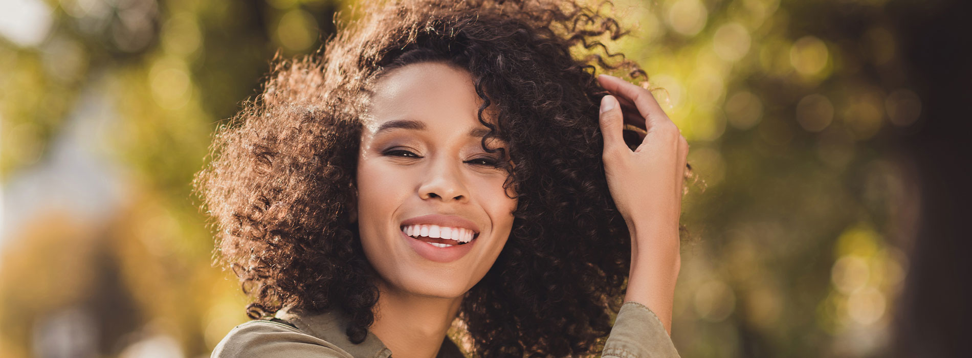 The image is a photograph of a woman with light skin, smiling at the camera. She appears to be in her late twenties or early thirties and has long hair. Her eyes are looking directly at the camera, and she is holding up her index finger near her mouth as if she s making a point or emphasizing something. The background is plain and light-colored, which suggests that this could be a stock photo used for various purposes such as advertising, personal branding, or lifestyle content.