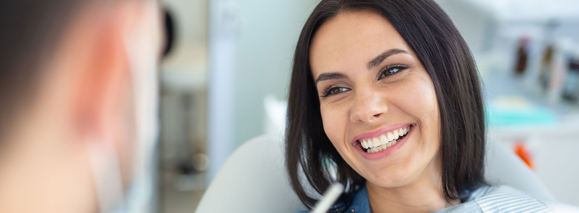 A person is seated in a dental chair, receiving care from a dental professional who stands behind them.